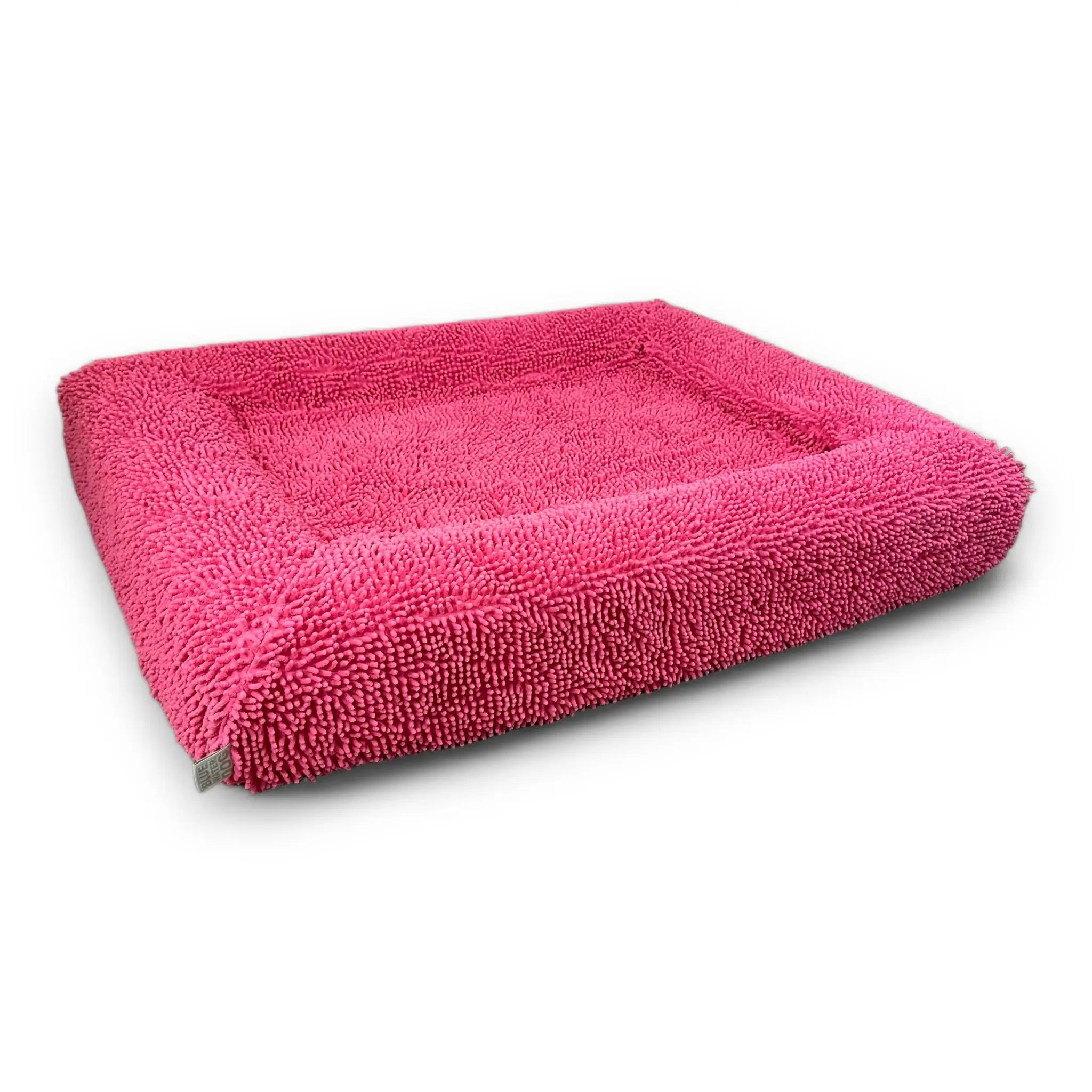 Side of a pink-colored shaggy towel cover on top of an orthopedic memory foam rectangular dog bed with bolsters.