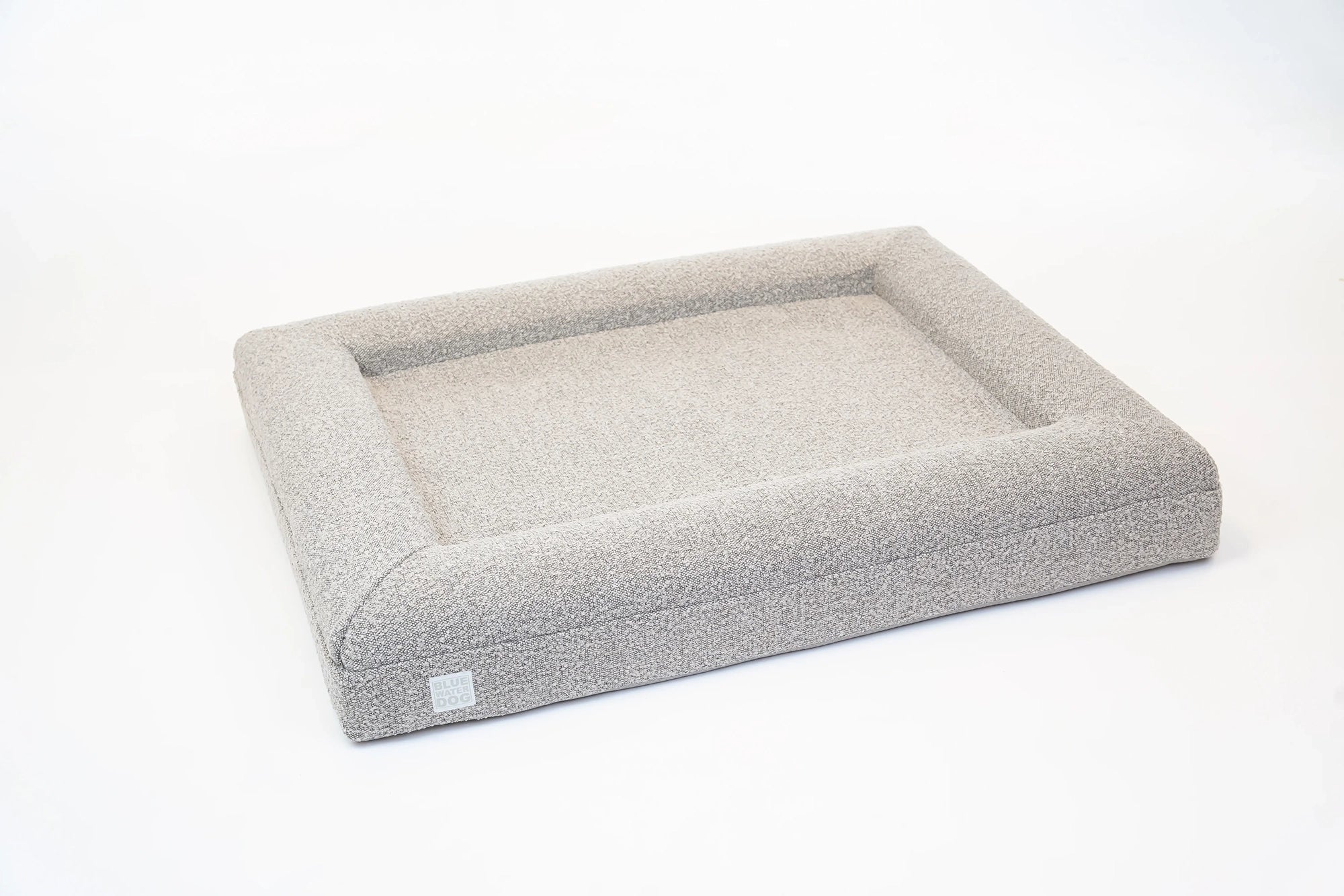 Side of a large, sand-colored orthopedic memory foam boucle dog bed with bolsters.