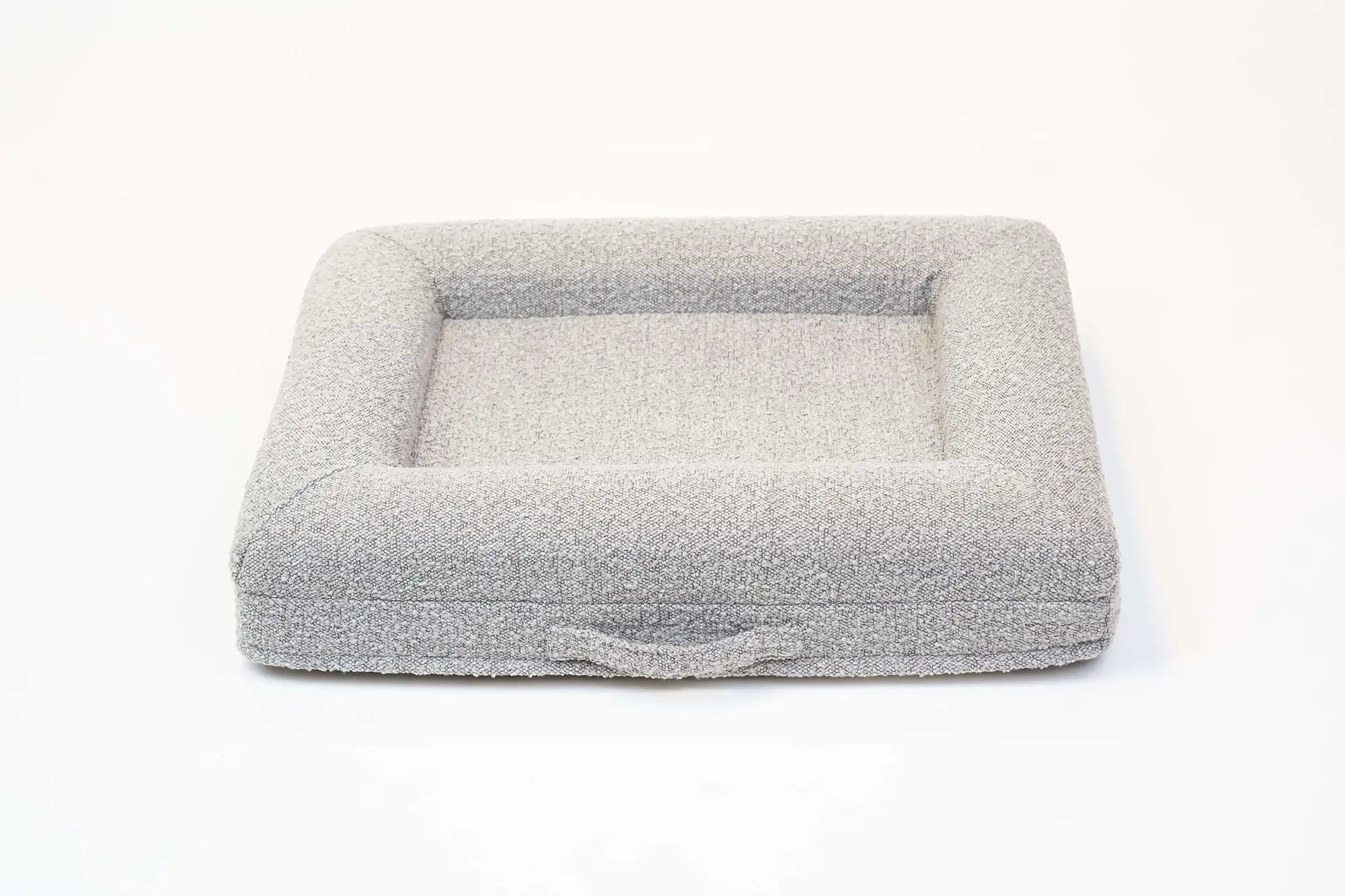 Back of a small, sand-colored orthopedic memory foam boucle dog bed with bolsters and a handle for easy transport.