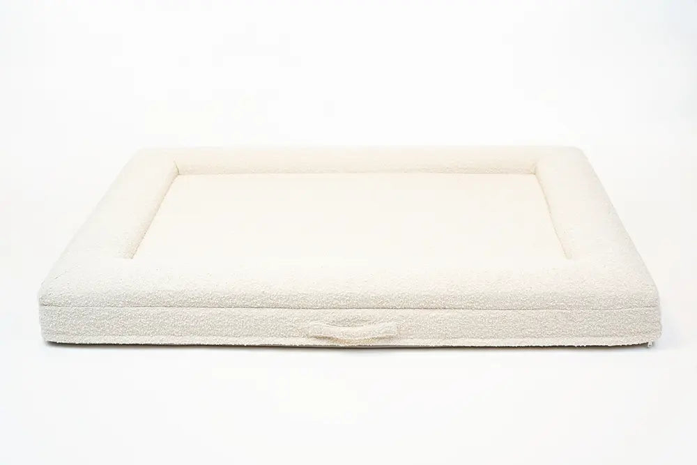 Back of an extra large, cloud-colored orthopedic memory foam boucle dog bed with bolsters and a handle for easy transport.