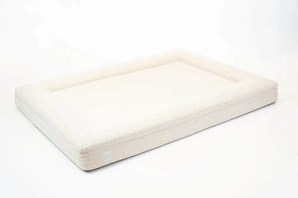 Side of an extra large, cloud-colored orthopedic memory foam boucle dog bed with bolsters.