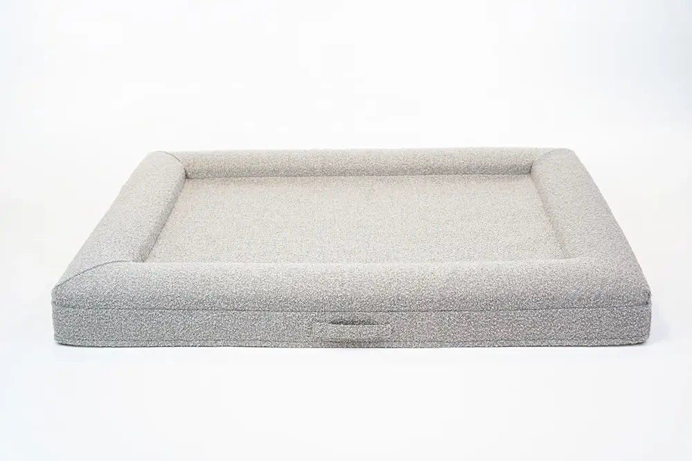 Back of an extra large, sand-colored orthopedic memory foam boucle dog bed with bolsters and a handle for easy transport.
