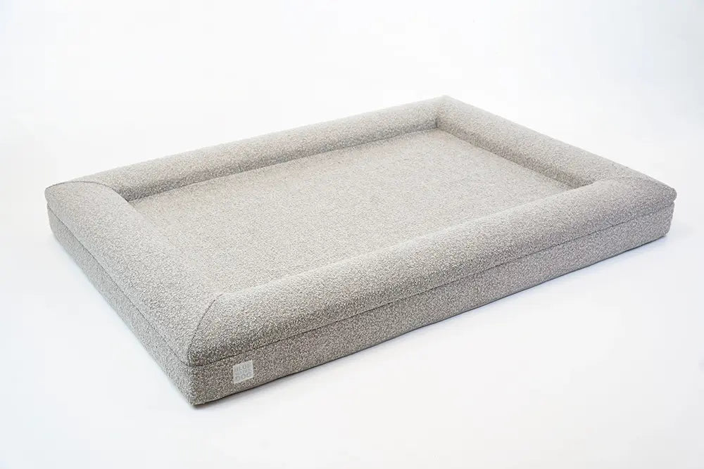 Side of an extra large, sand-colored orthopedic memory foam boucle dog bed with bolsters.