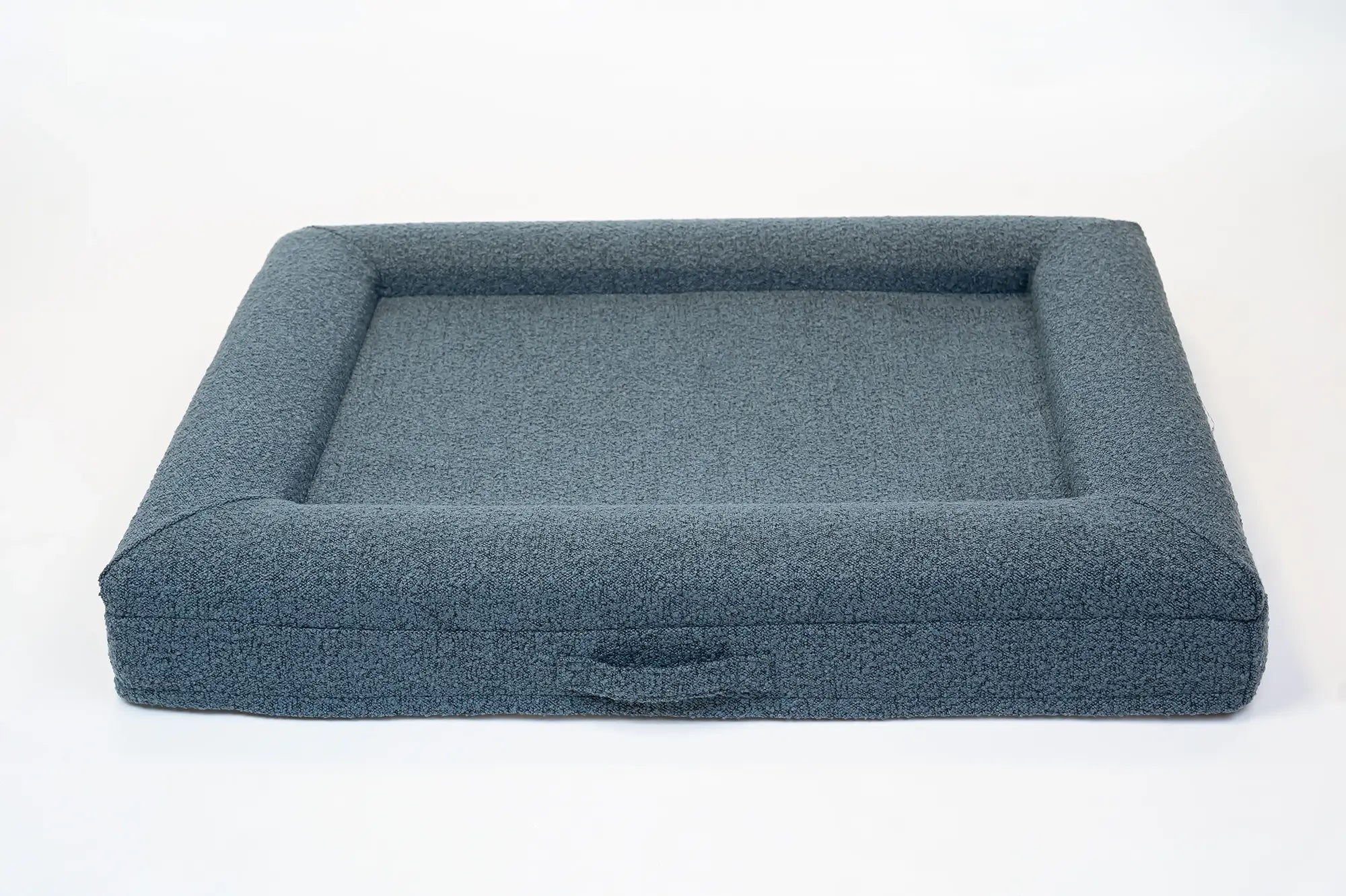 Back of a large, ocean blue-colored orthopedic memory foam boucle dog bed with bolsters and a handle for easy transport.