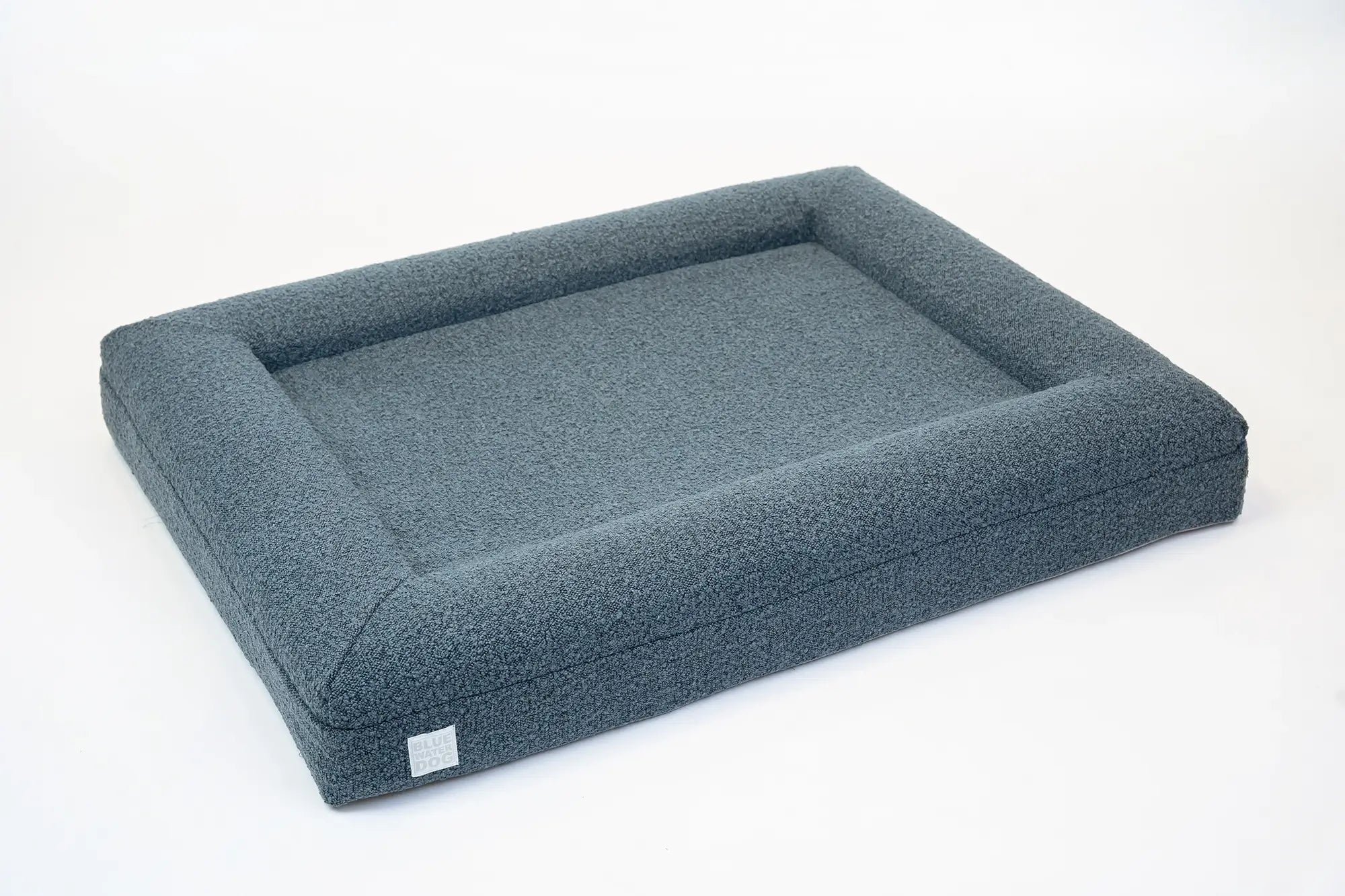 Side of a large, blue-colored orthopedic memory foam boucle dog bed with bolsters.