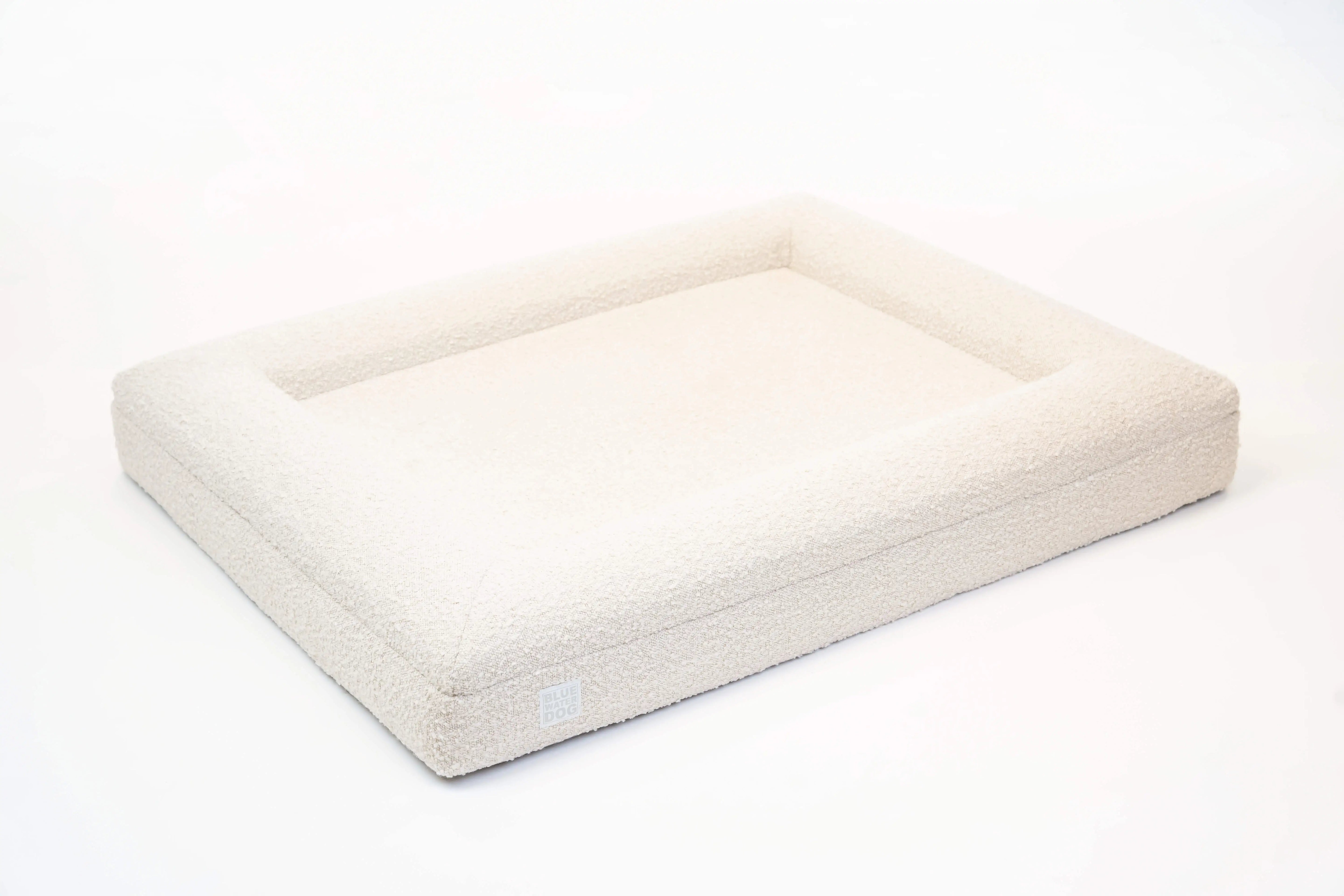 Side of a large, cloud-colored orthopedic memory foam boucle dog bed with bolsters.
