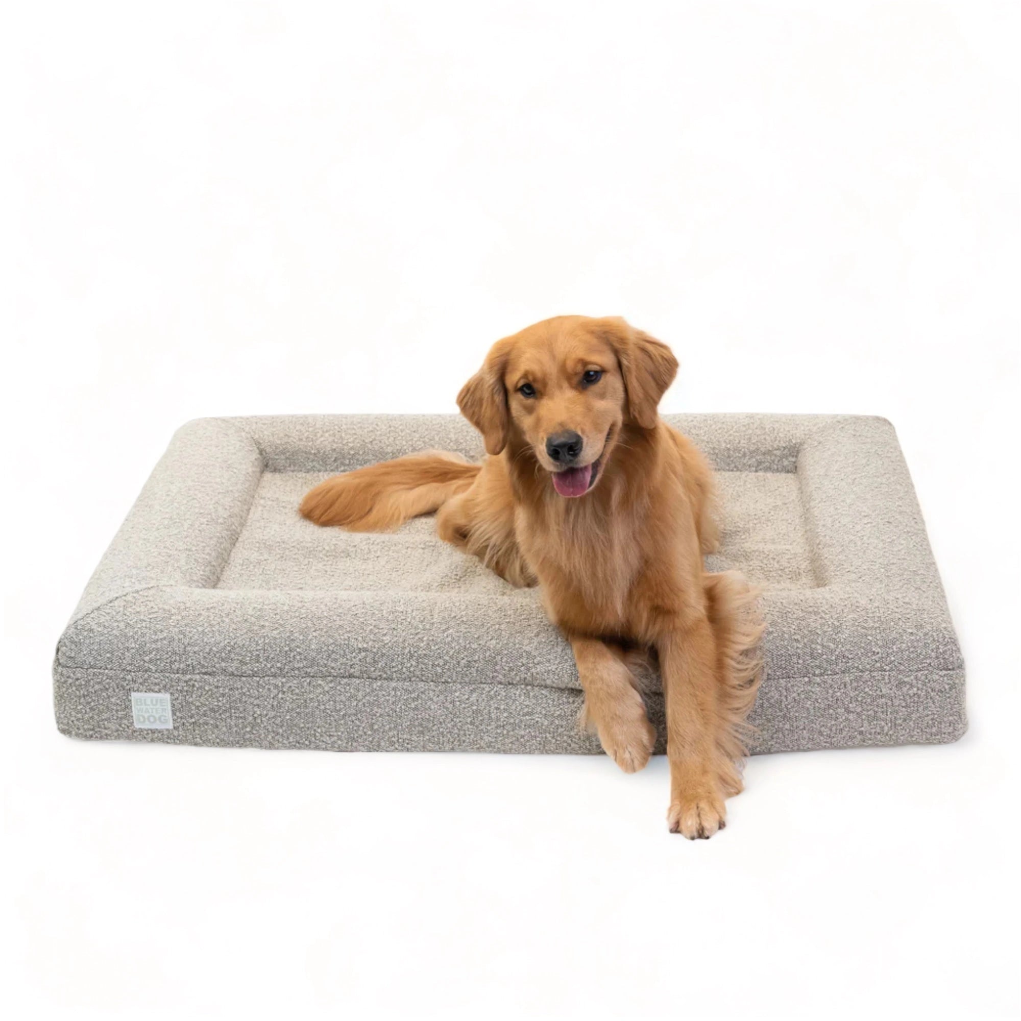 Golden Retriever laying on a large, sand-colored orthopedic memory foam rectangular boucle dog bed with bolsters.