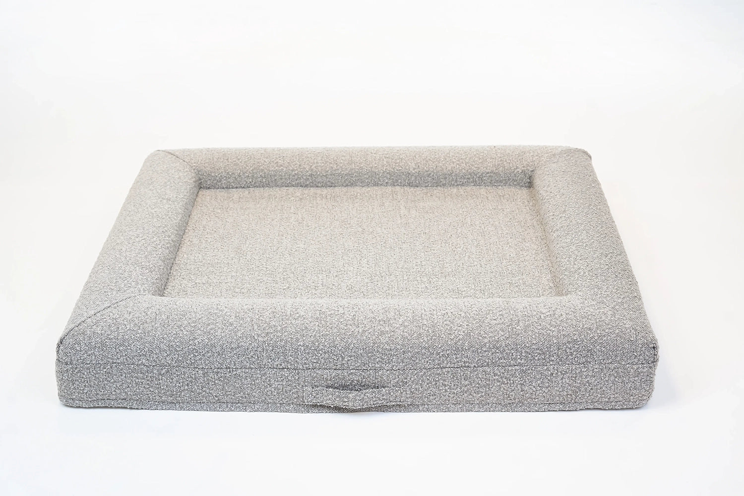 Back of a large, sand-colored orthopedic memory foam boucle dog bed with bolsters and a handle for easy transport.