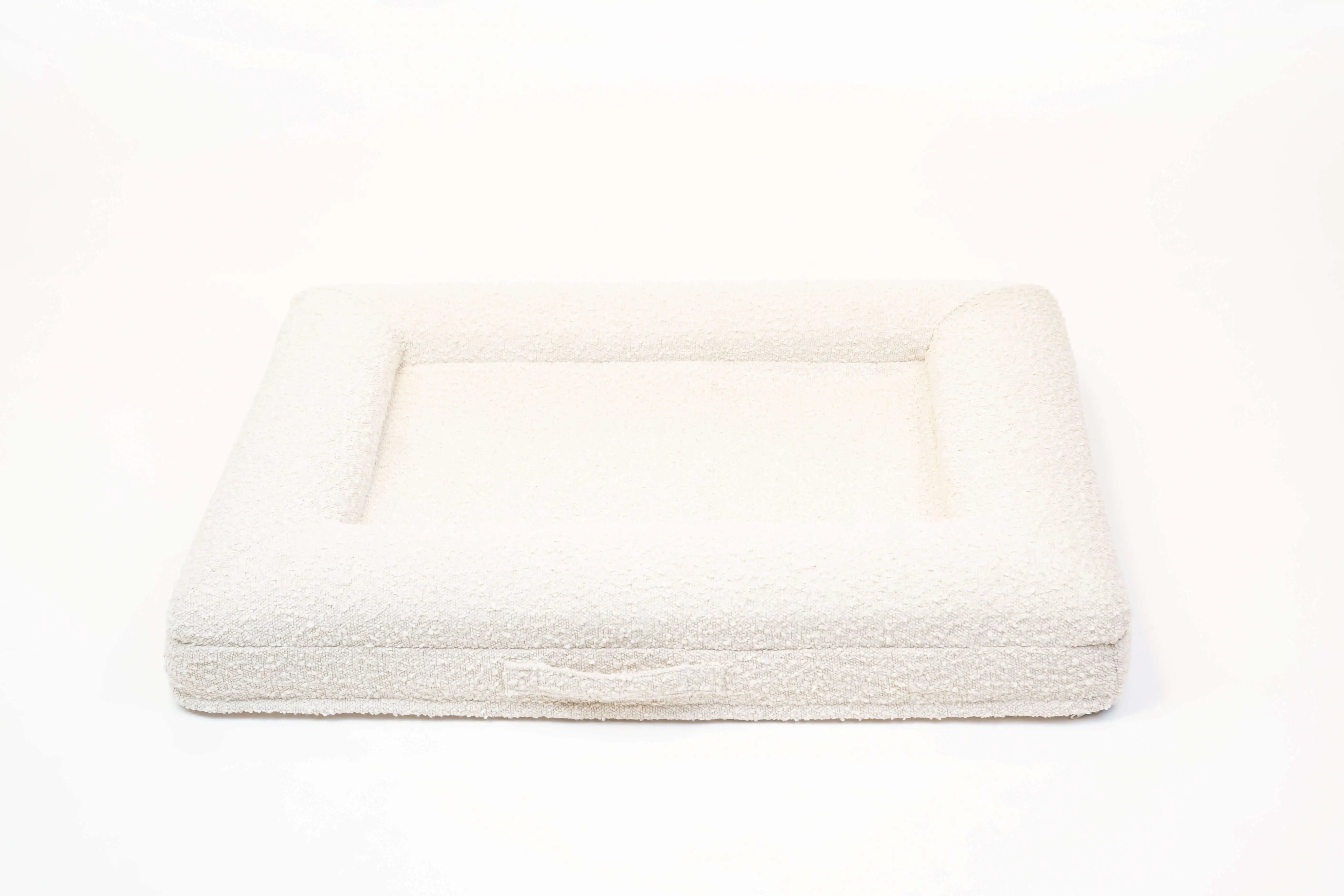 Back of a medium, cloud-colored orthopedic memory foam boucle dog bed with bolsters and a handle for easy transport