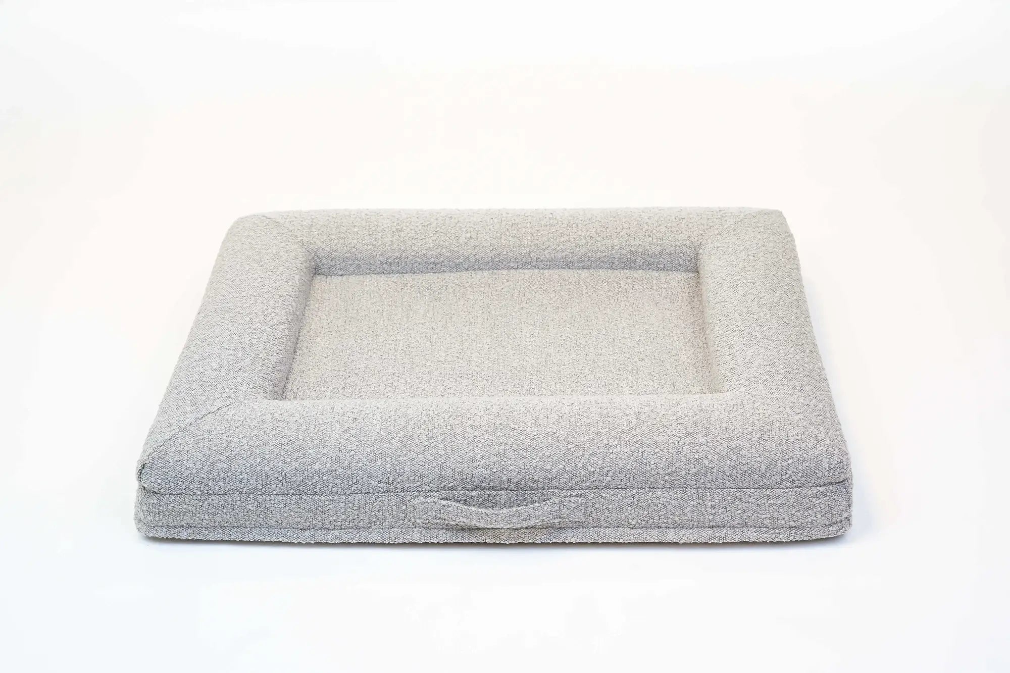 Back of a medium, sand-colored orthopedic memory foam boucle dog bed with bolsters and a handle for easy transport.