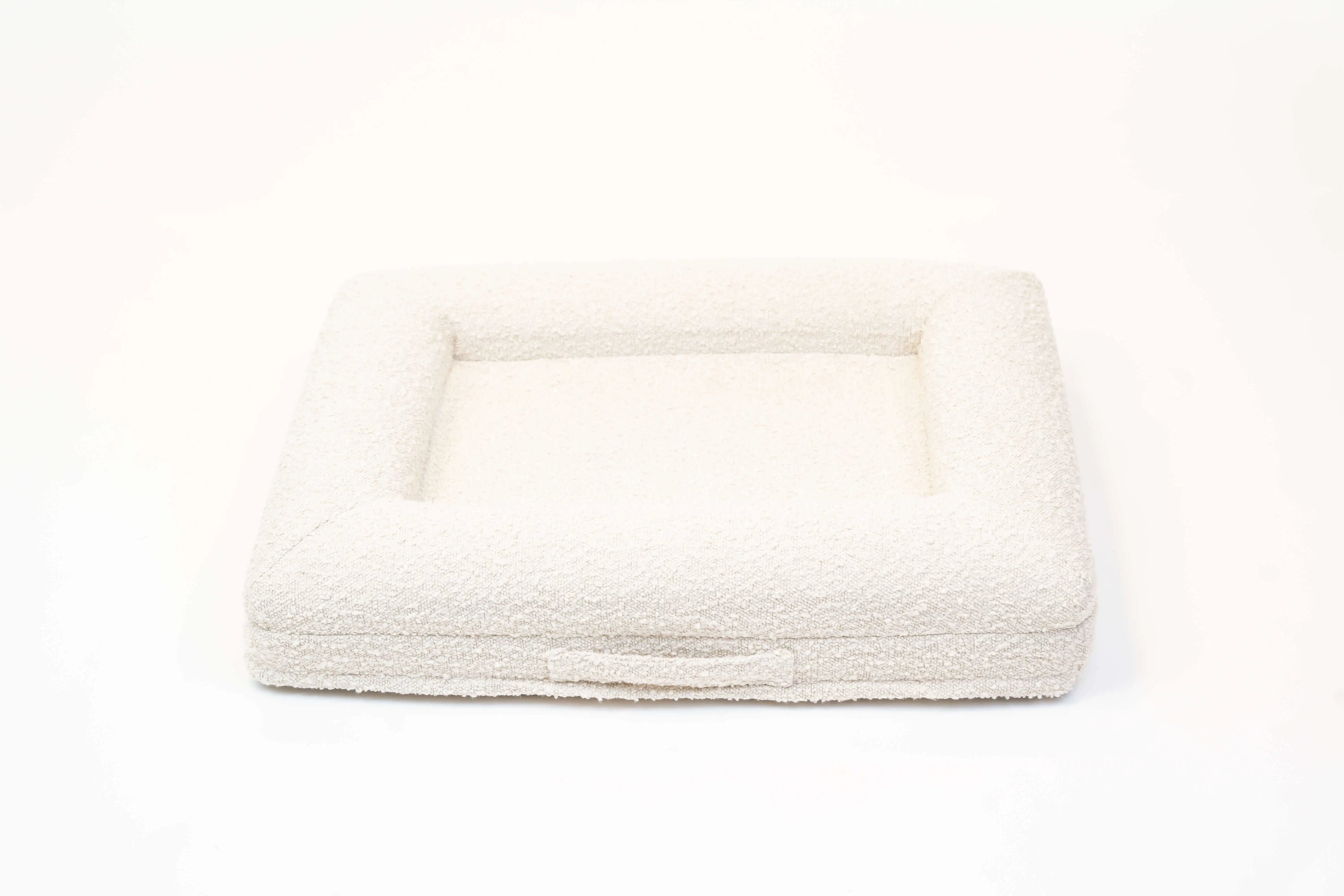 Back of a small, cloud-colored orthopedic memory foam boucle dog bed with bolsters and a handle for easy transport