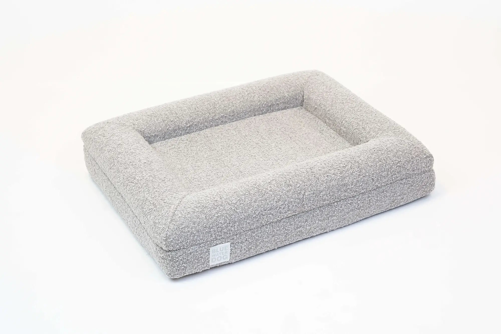 Side of a small, sand-colored orthopedic memory foam boucle dog bed with bolsters.